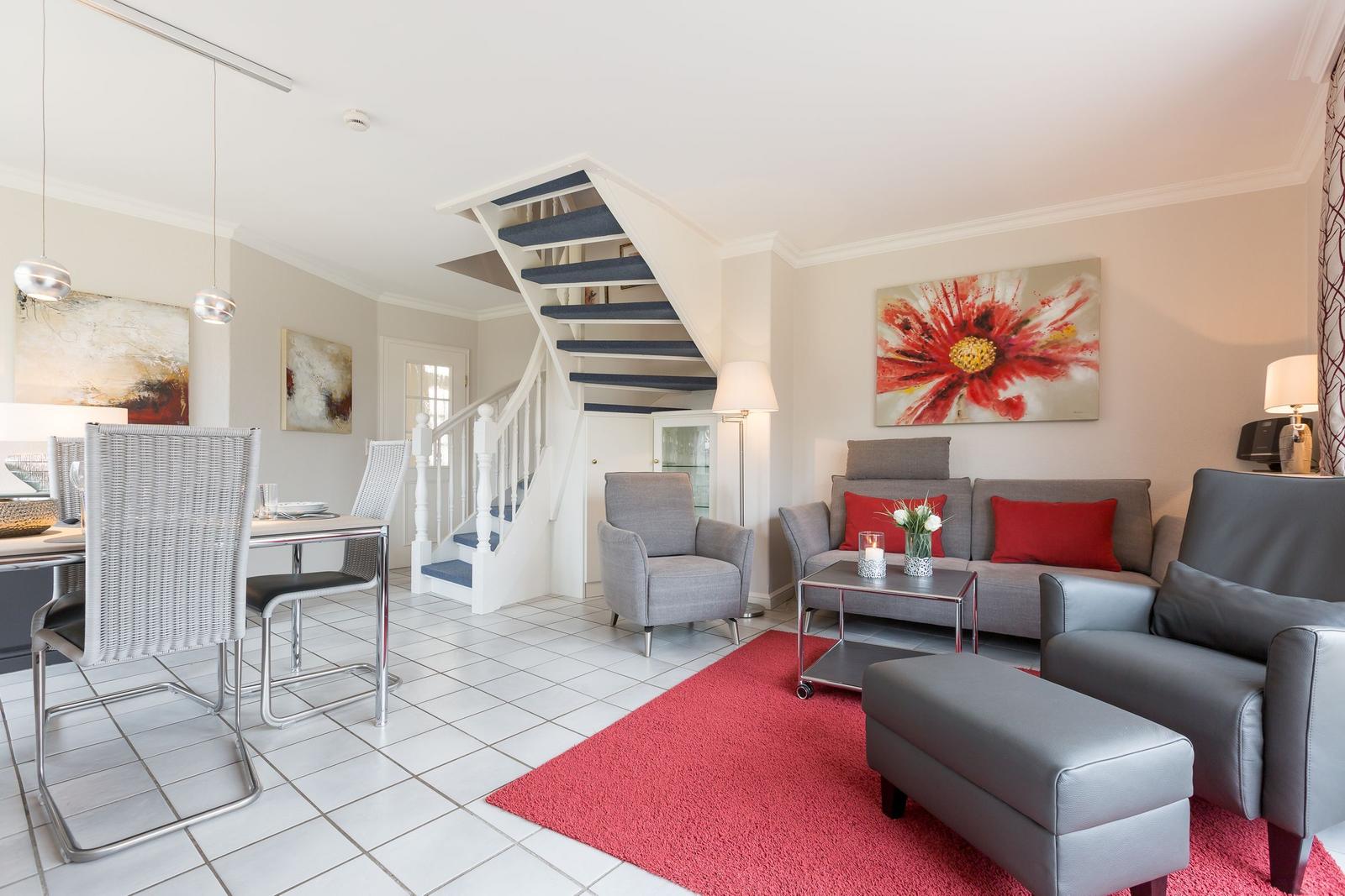 Living and dining area with staircase, sofa, armchairs, and red rug.