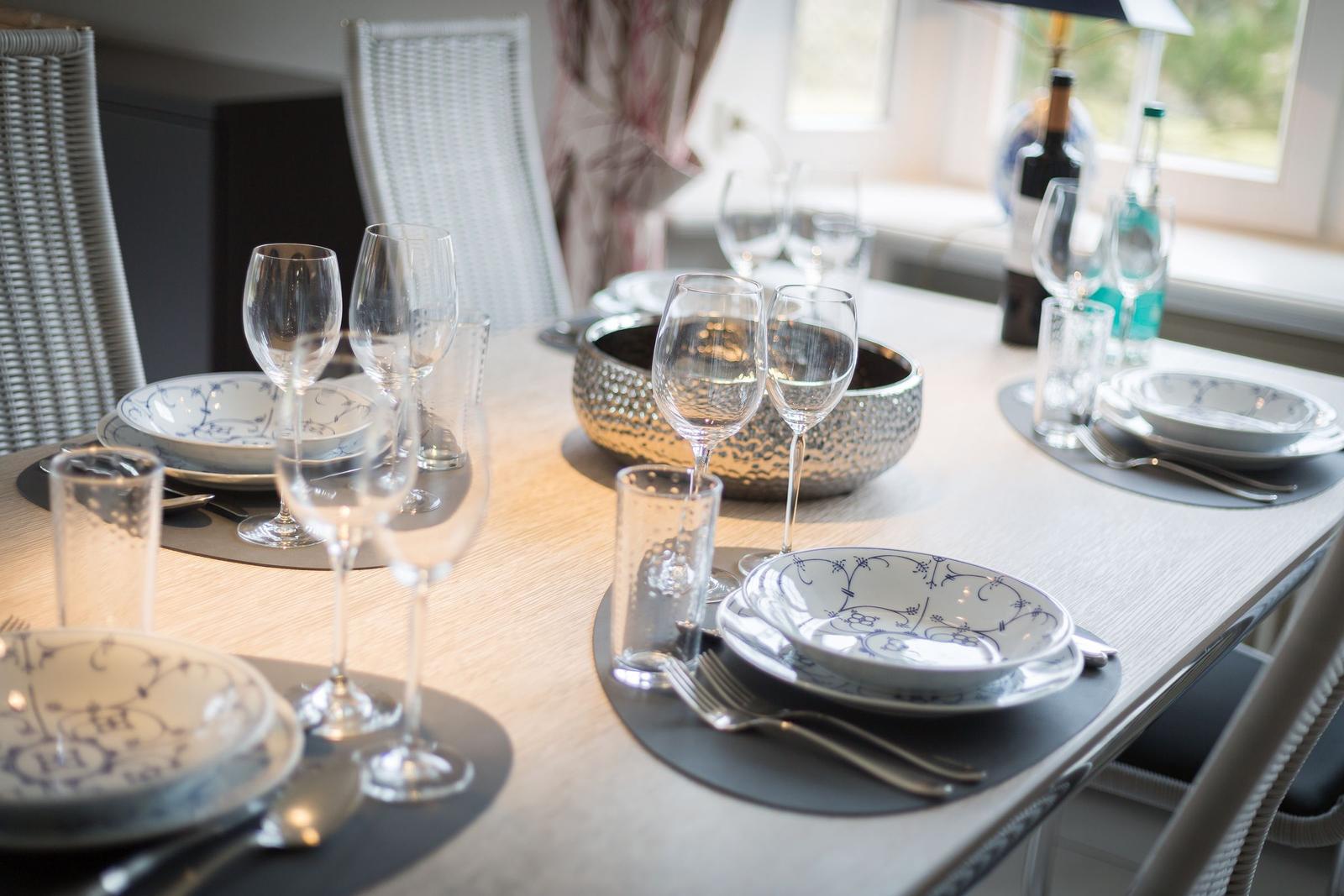 Dining table with dishes, glasses, and chairs. Window with view outside.