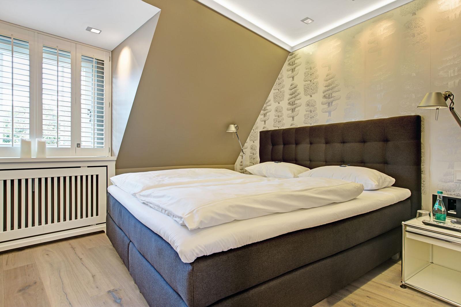 Schlafzimmer mit Doppelbett, Fenster mit Jalousien und Wand mit Baum-Motivtapete.