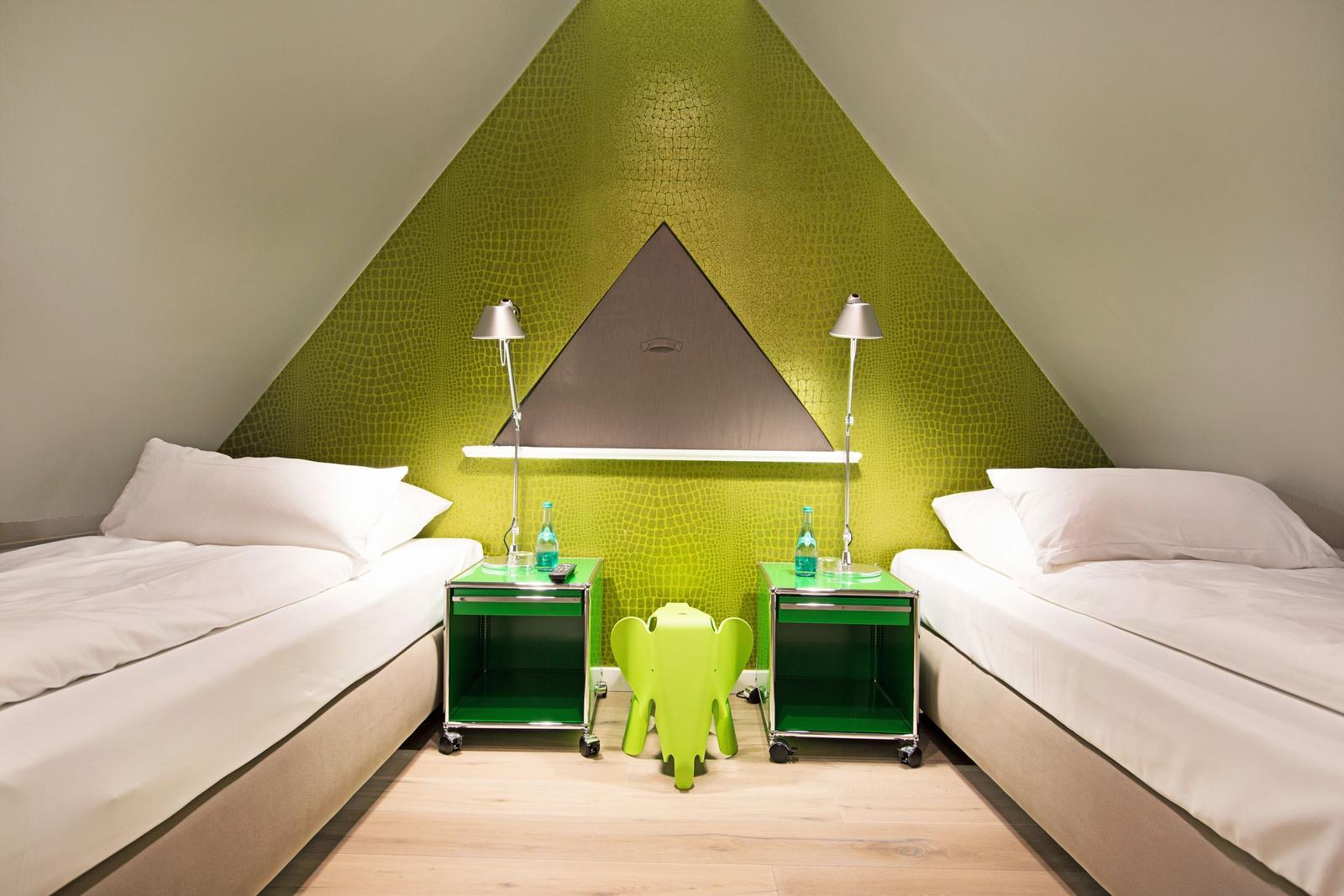 Zwei Betten mit Nachttischen und grüner Wand im Dachgeschosszimmer.