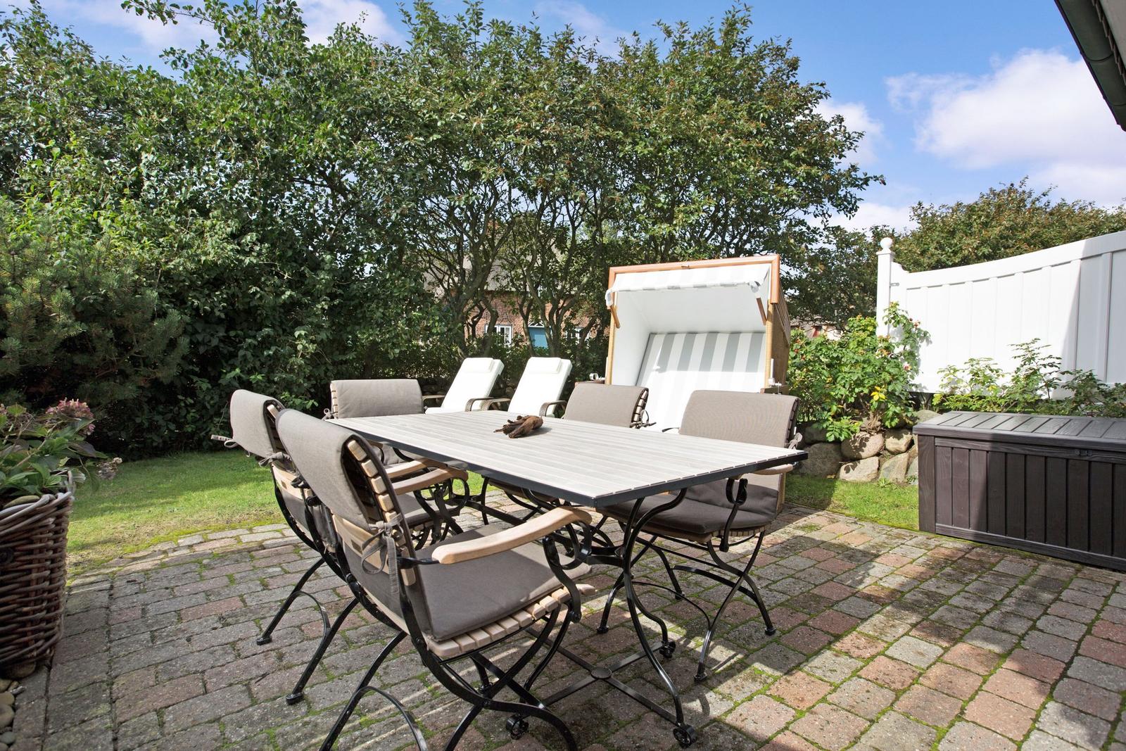 Terrasse mit Tisch, Stühlen und Liege unter Bäumen.