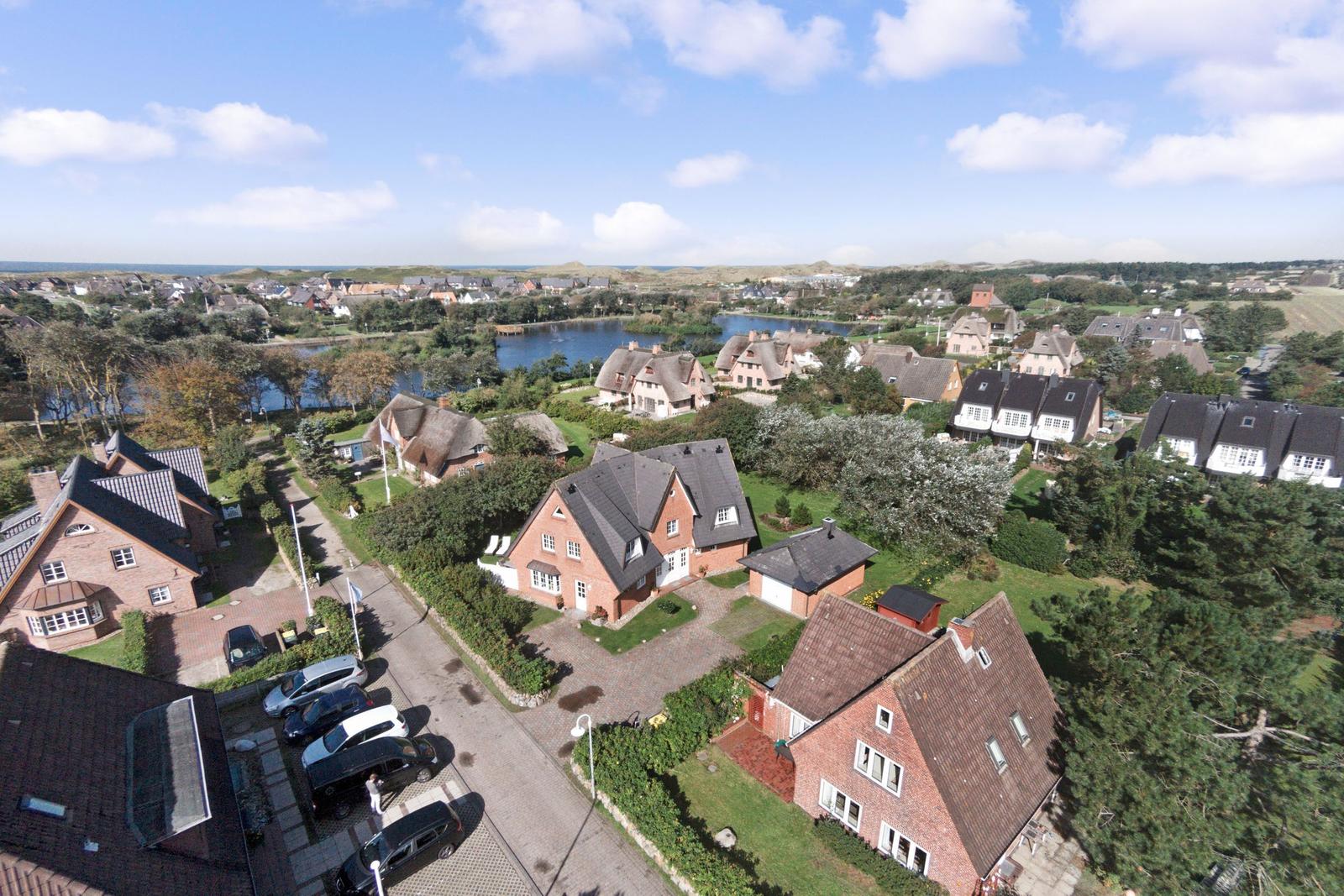 Aerial view of a village with houses, a lake, and dunes in the background.
