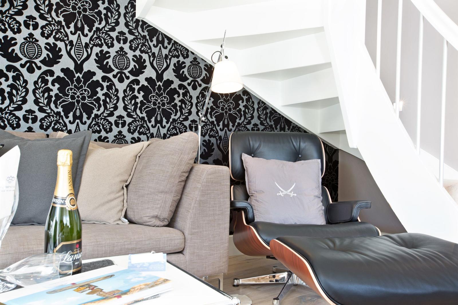 Sitzbereich unter Treppe mit Sofa und Ledersessel. Wand mit Muster, Flasche Champagner.