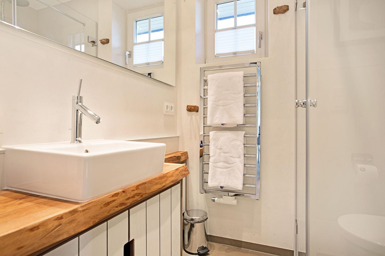 Badezimmer mit Waschbecken, Spiegel, Handtuchhalter und Dusche.