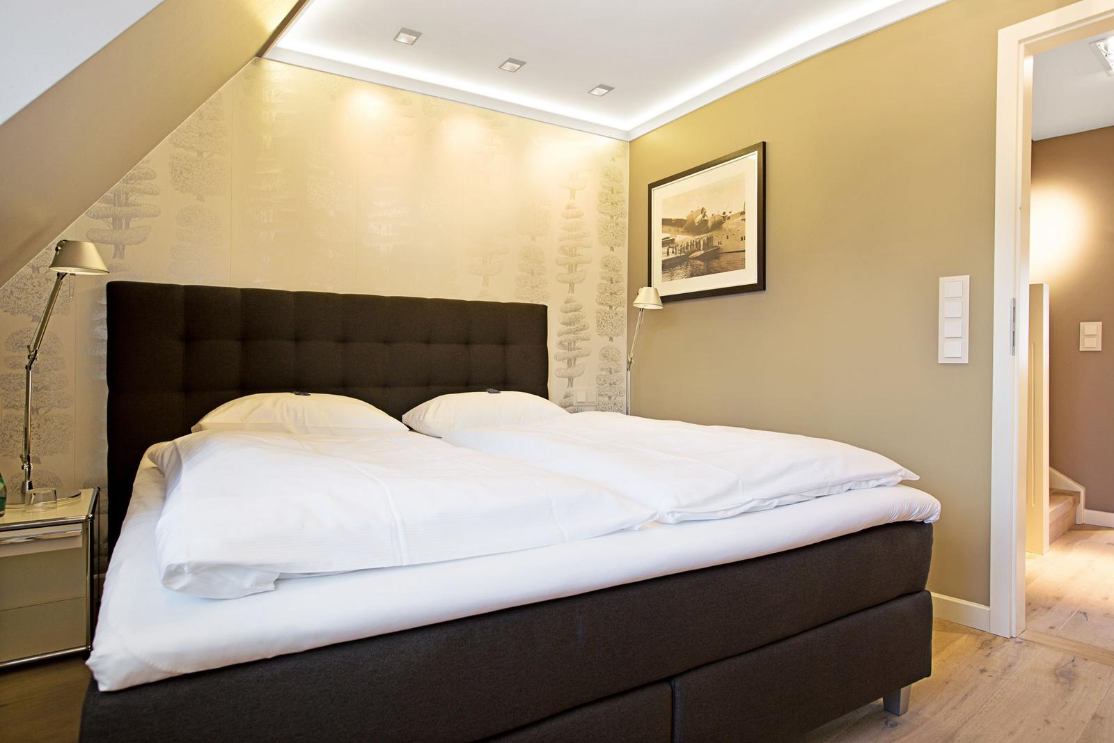 Schlafzimmer mit Doppelbett, Wandbild und Stehlampe.