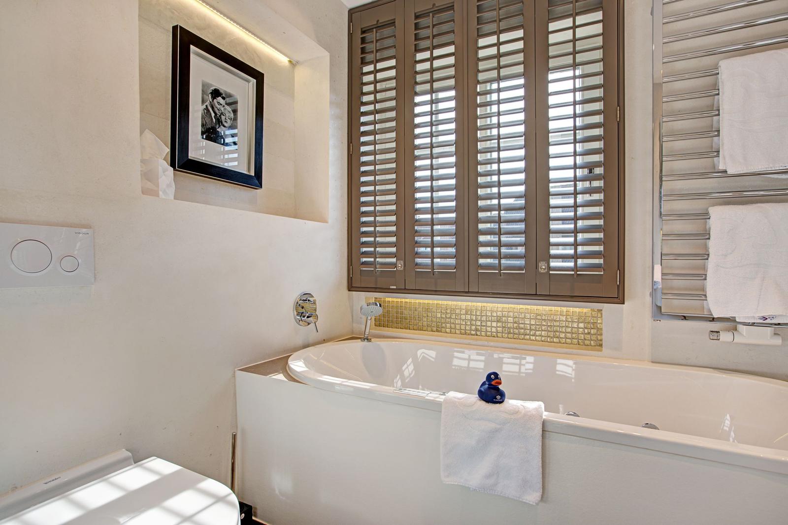 Bad mit Badewanne, Fenster mit Jalousien und Handtuchhalter.