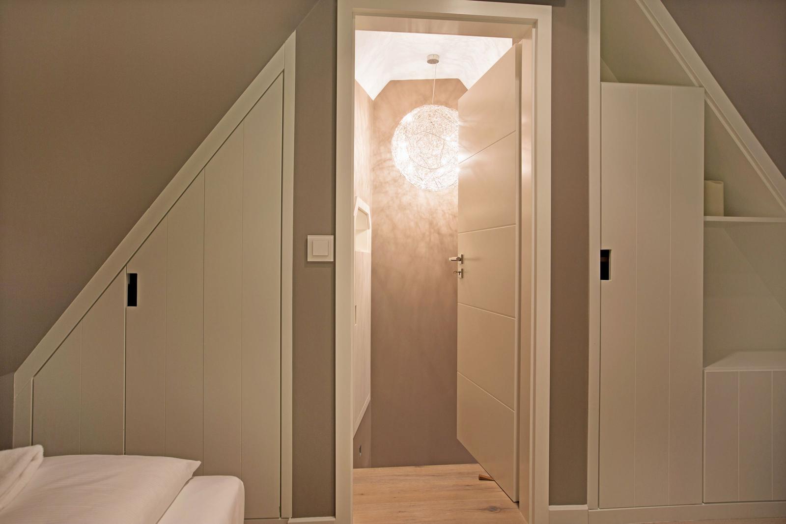 Schlafzimmer mit Dachschrägen und integriertem Schrank. Durchgang zur hängenden Lampe.
