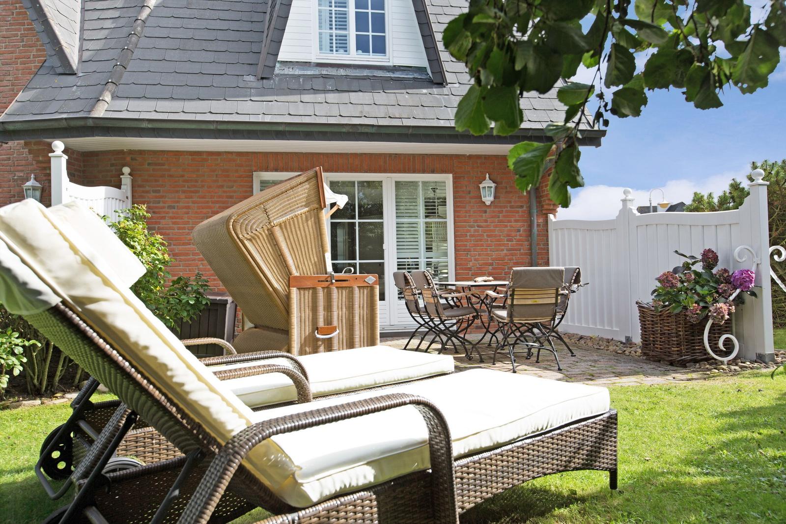 Garten mit Liegestühlen, Tisch und Stühlen vor einem Haus mit rotem Backstein und weißem Zaun.