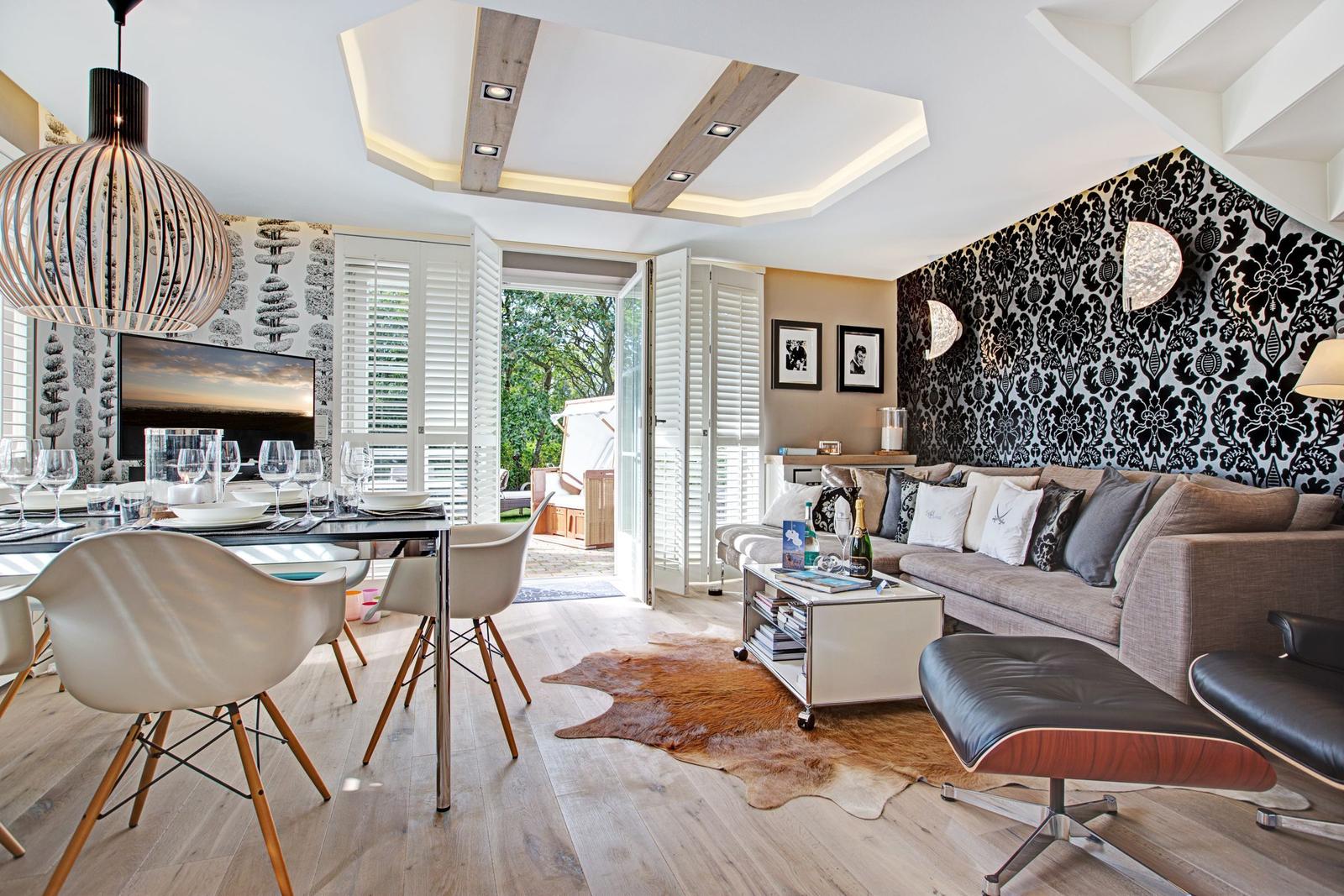 Wohn- und Essbereich mit Sofa, Tisch und Stühlen. Hintergrund mit Tapete und Fenster zur Terrasse.