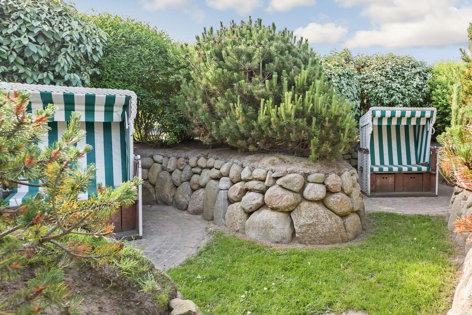 Two beach chairs with green-white stripes stand in the garden next to a stone wall.