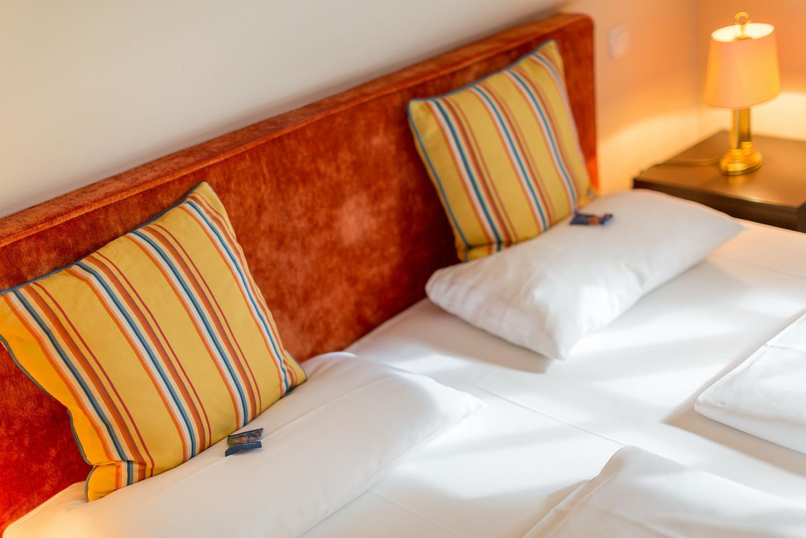 Double bed with white sheets and striped pillows against a wooden headboard.