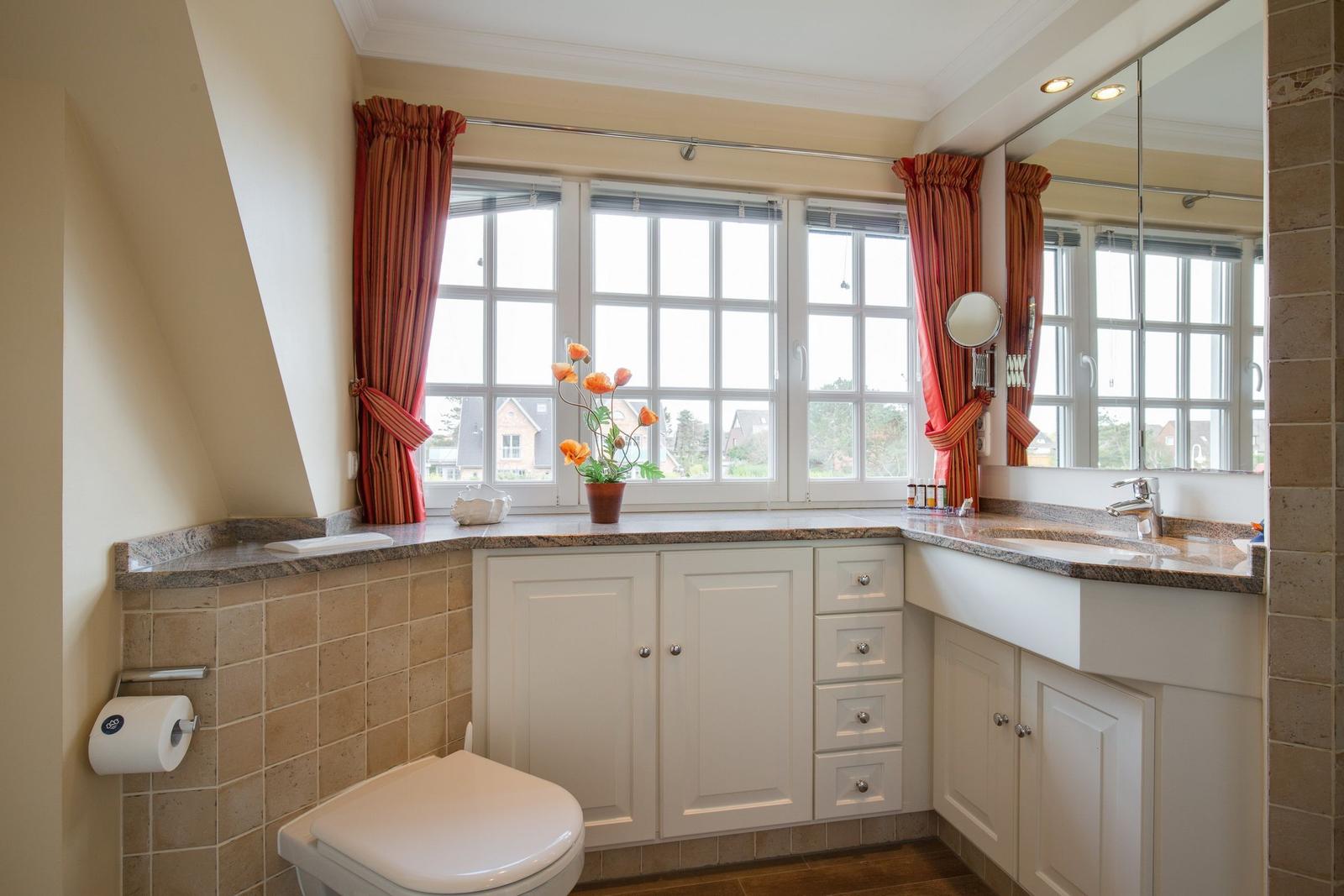 Bathroom with window, sink, and toilet. White cabinets and red curtains.