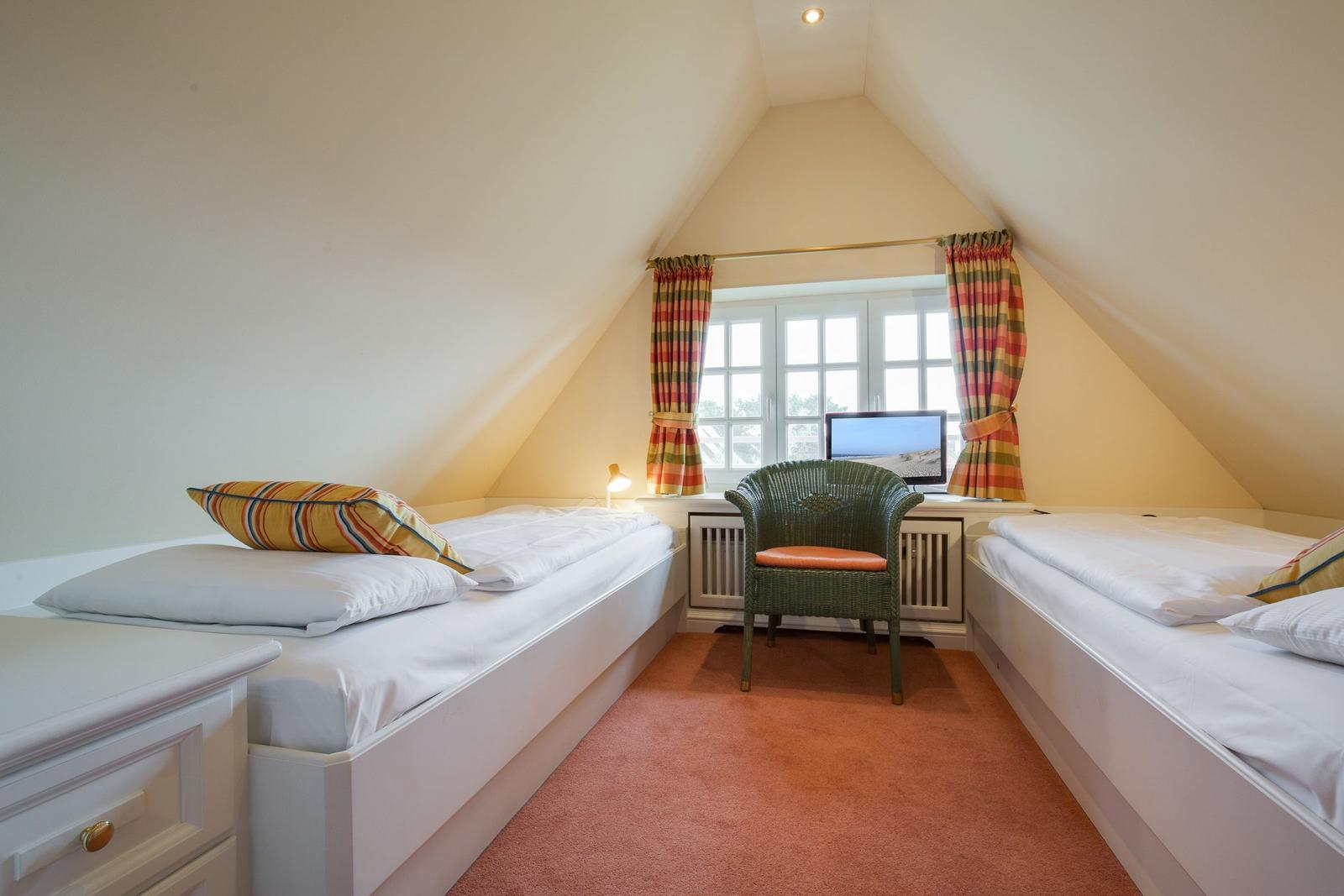 Two beds in an attic room with window and chair.