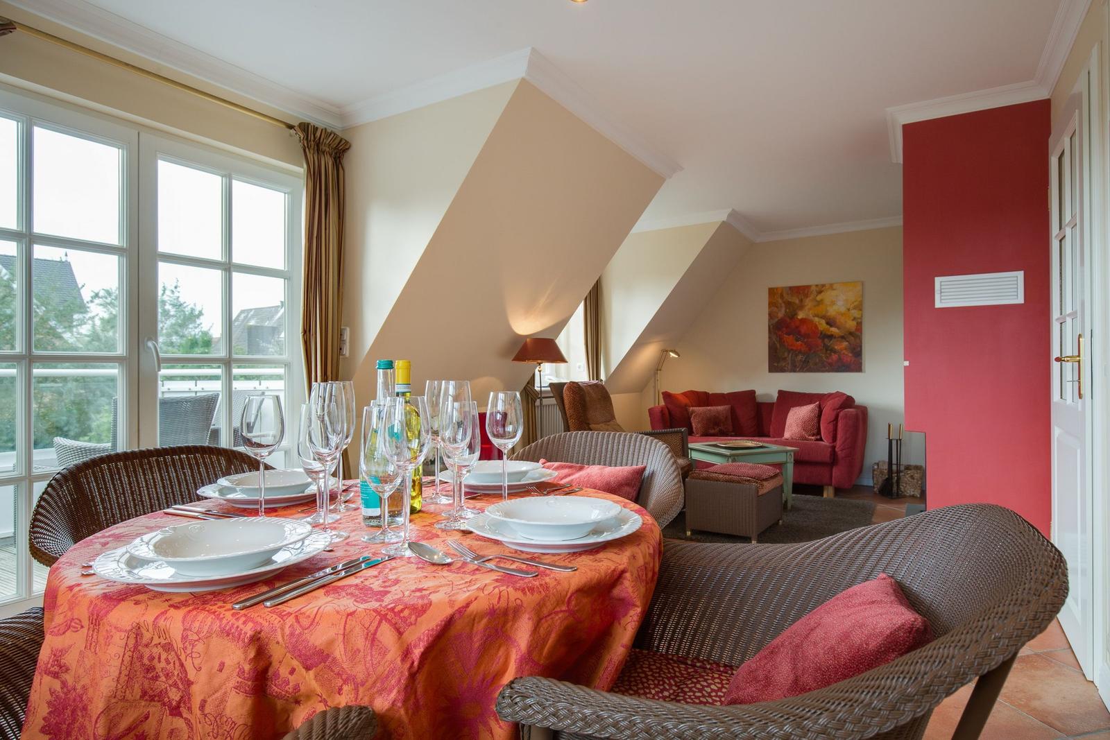 Dining table with tablecloth and glasses, living area with sofa and wall art.