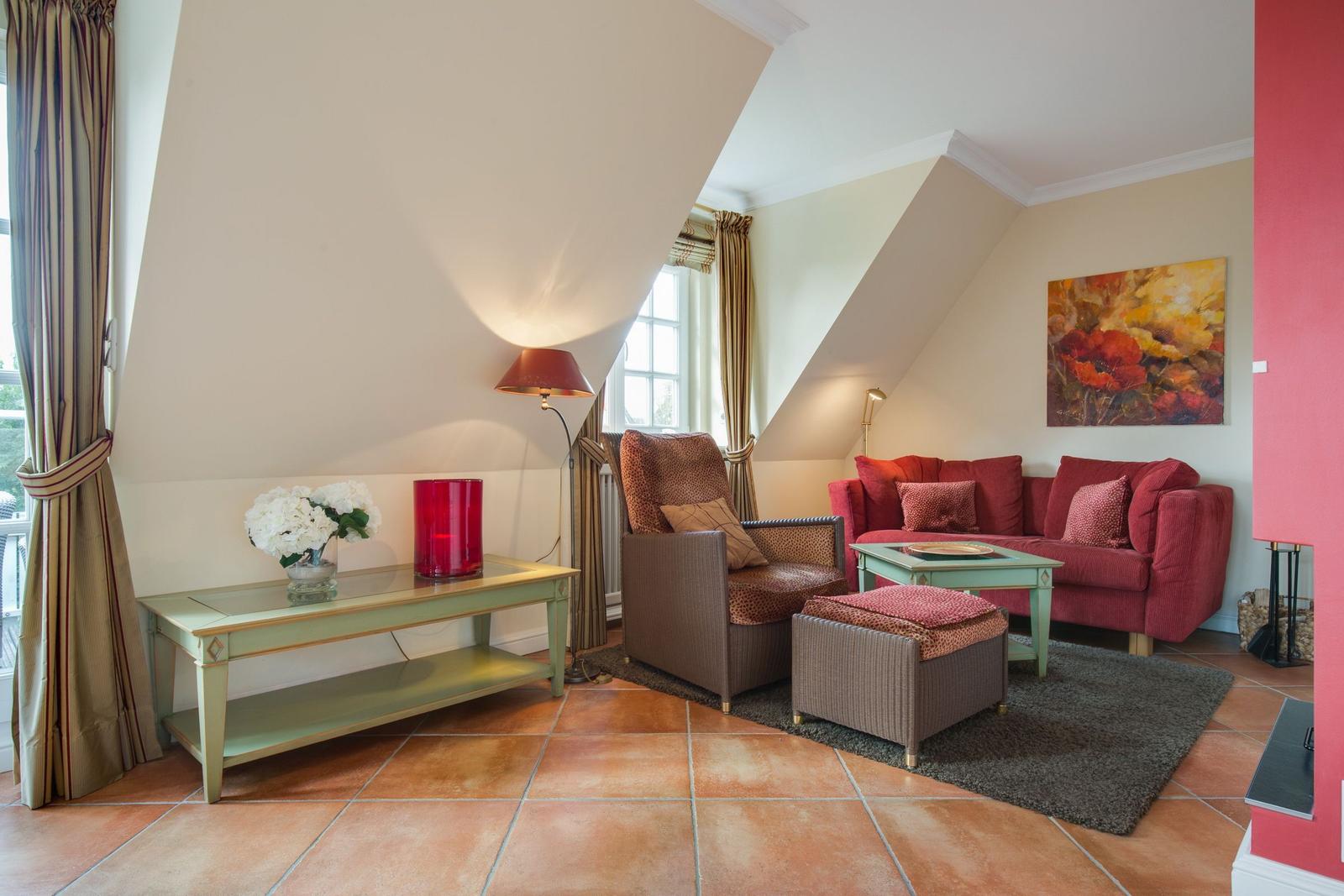 Living room with red sofa, armchair, and wooden table under sloped walls.