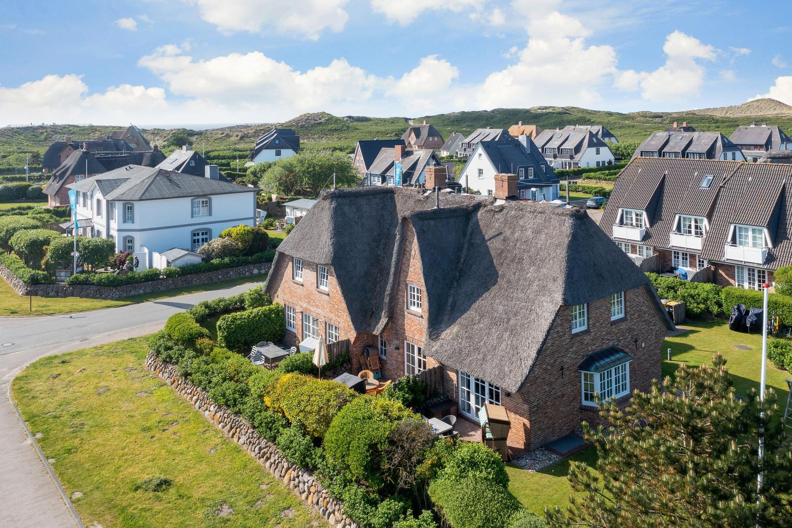 House with thatched roof and garden. Surroundings with other houses and hills.