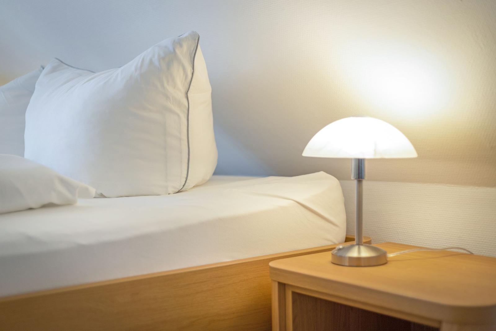 A bed with white pillows and a lamp on a wooden nightstand.