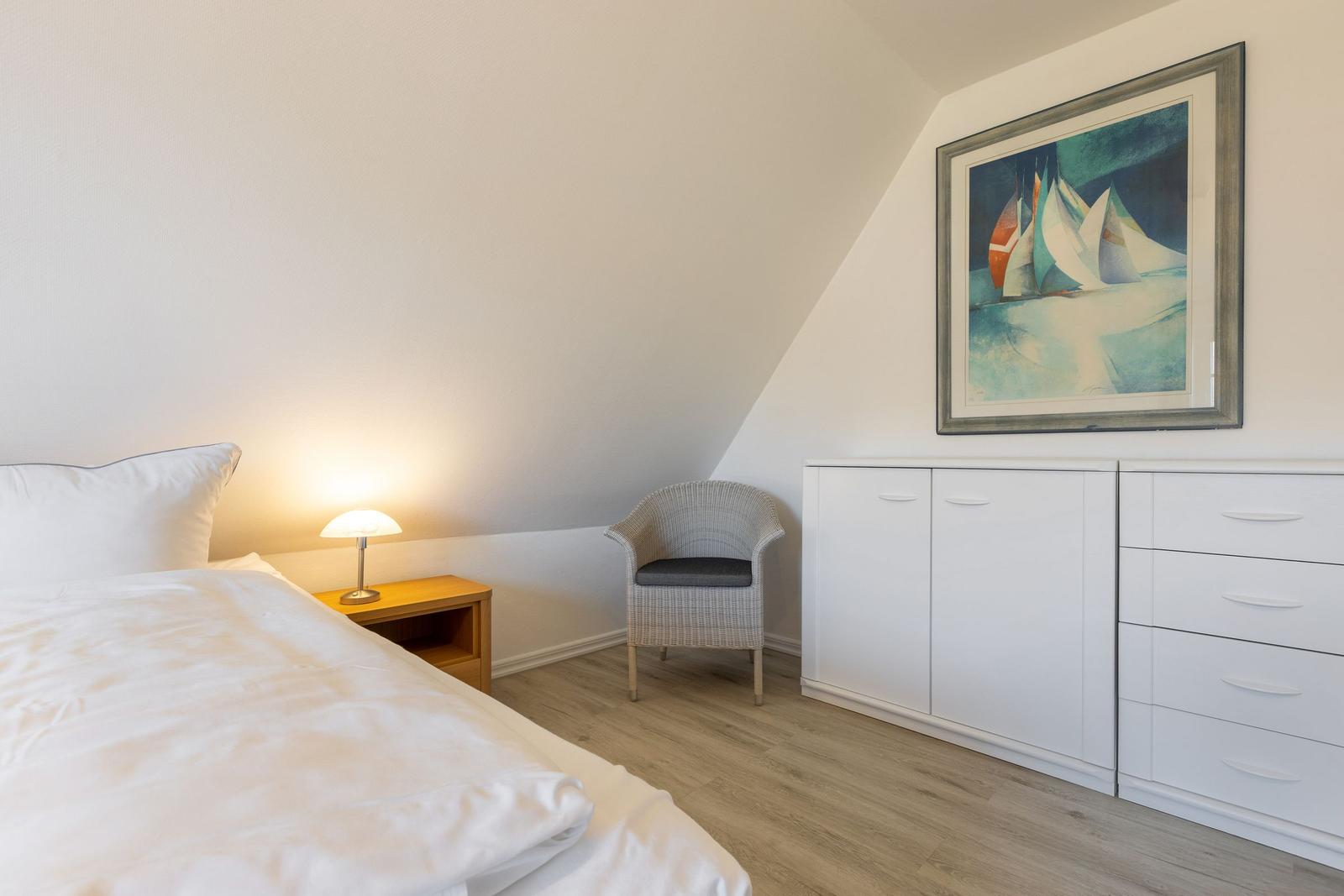 Bedroom with bed, nightstand, chair, and wardrobe under sloped ceiling.