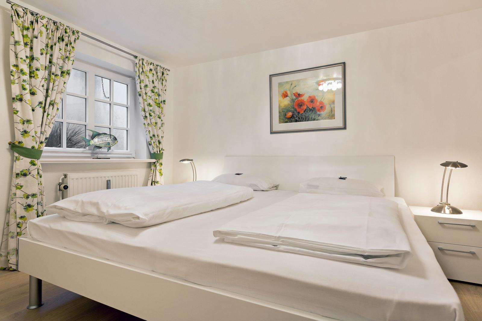 Bedroom with white bed, window with floral curtains, and wall art with poppies.