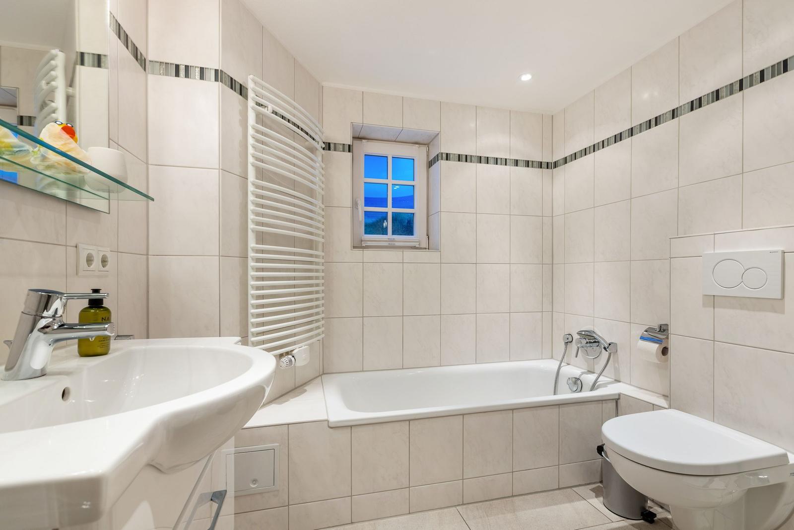 Bathroom with bathtub, toilet, and sink. Window shows view.