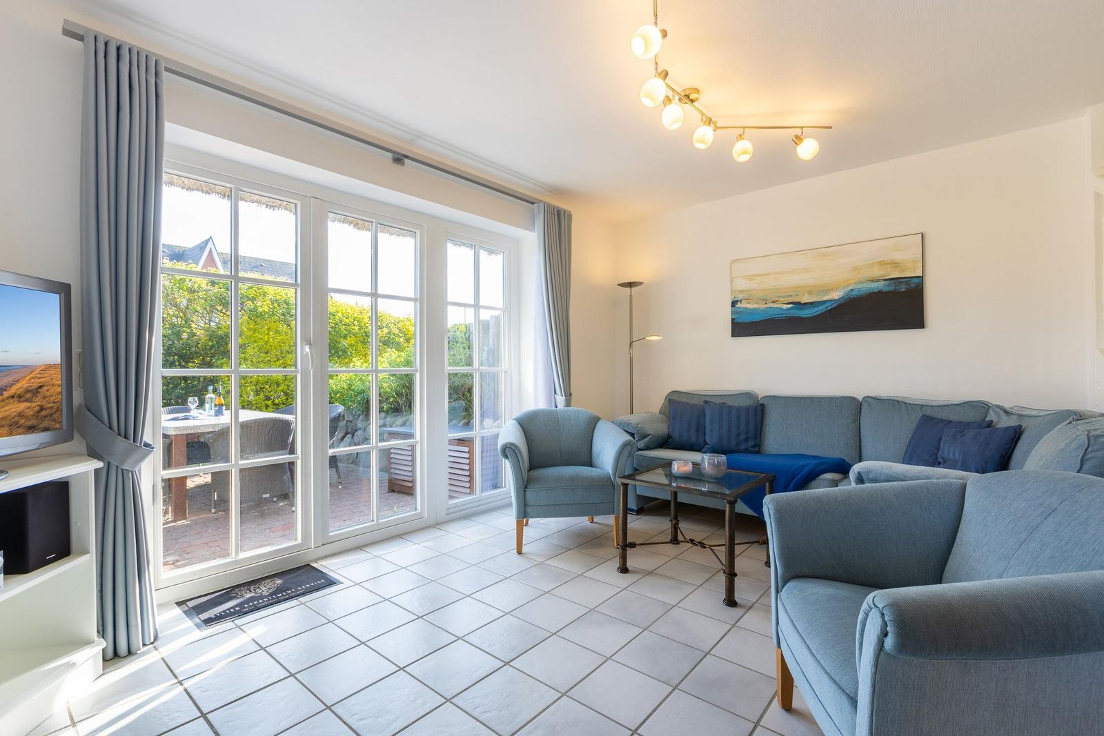 Living room with sofa, armchair, and terrace. Windows with gray curtains.