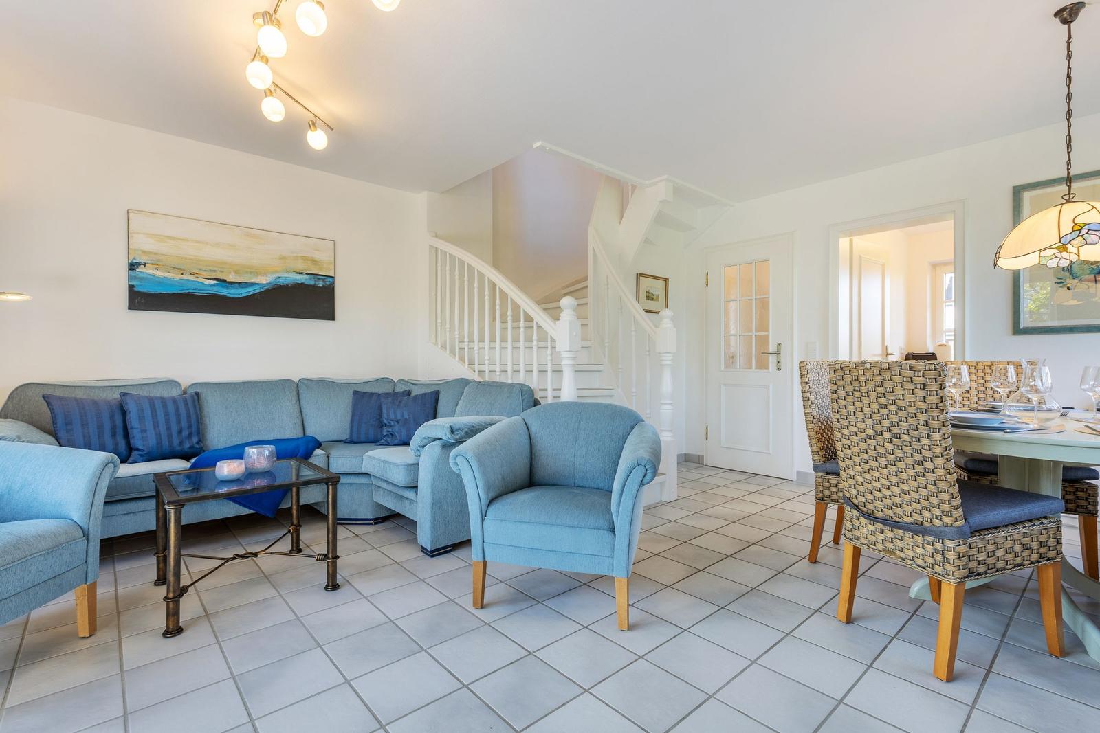 Living and dining area with blue sofa, staircase, and dining table with chairs.