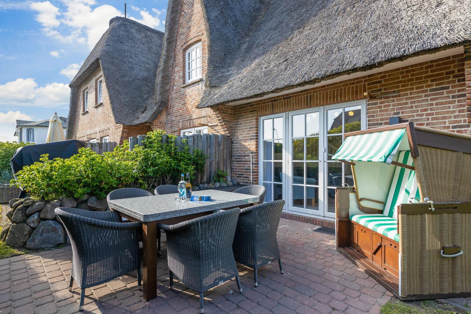 Terrace with table, chairs, and beach chair in front of a thatched-roof house.