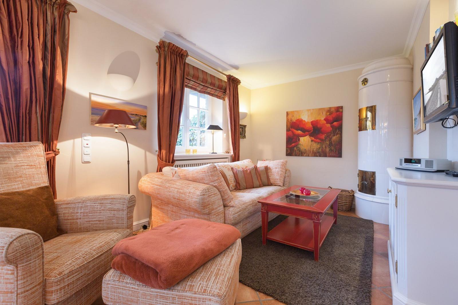 Living room with sofa, armchair, coffee table, and wood-burning stove. Window with curtains and wall painting.
