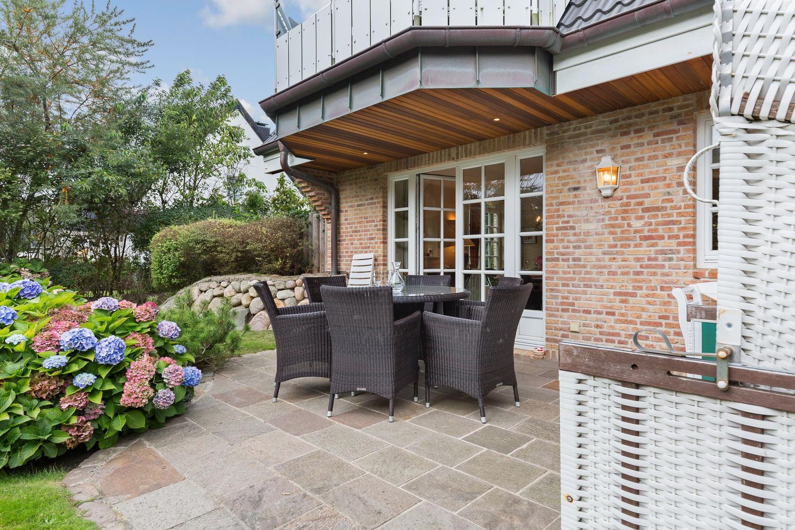 Terrace with seating group, flower bed and stone paving in front of a brick house.