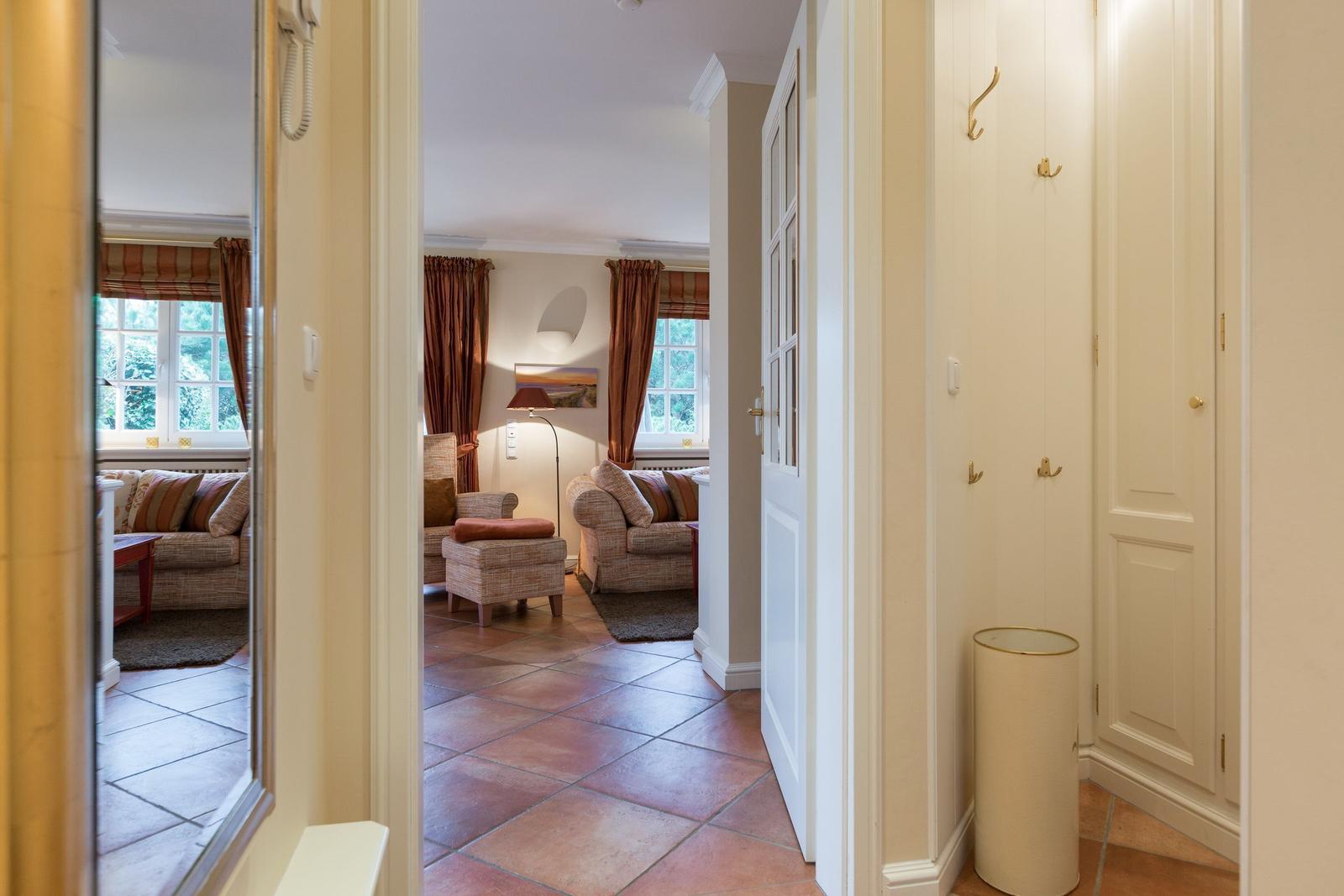 Hallway with hooks and view into living room with seating and windows.