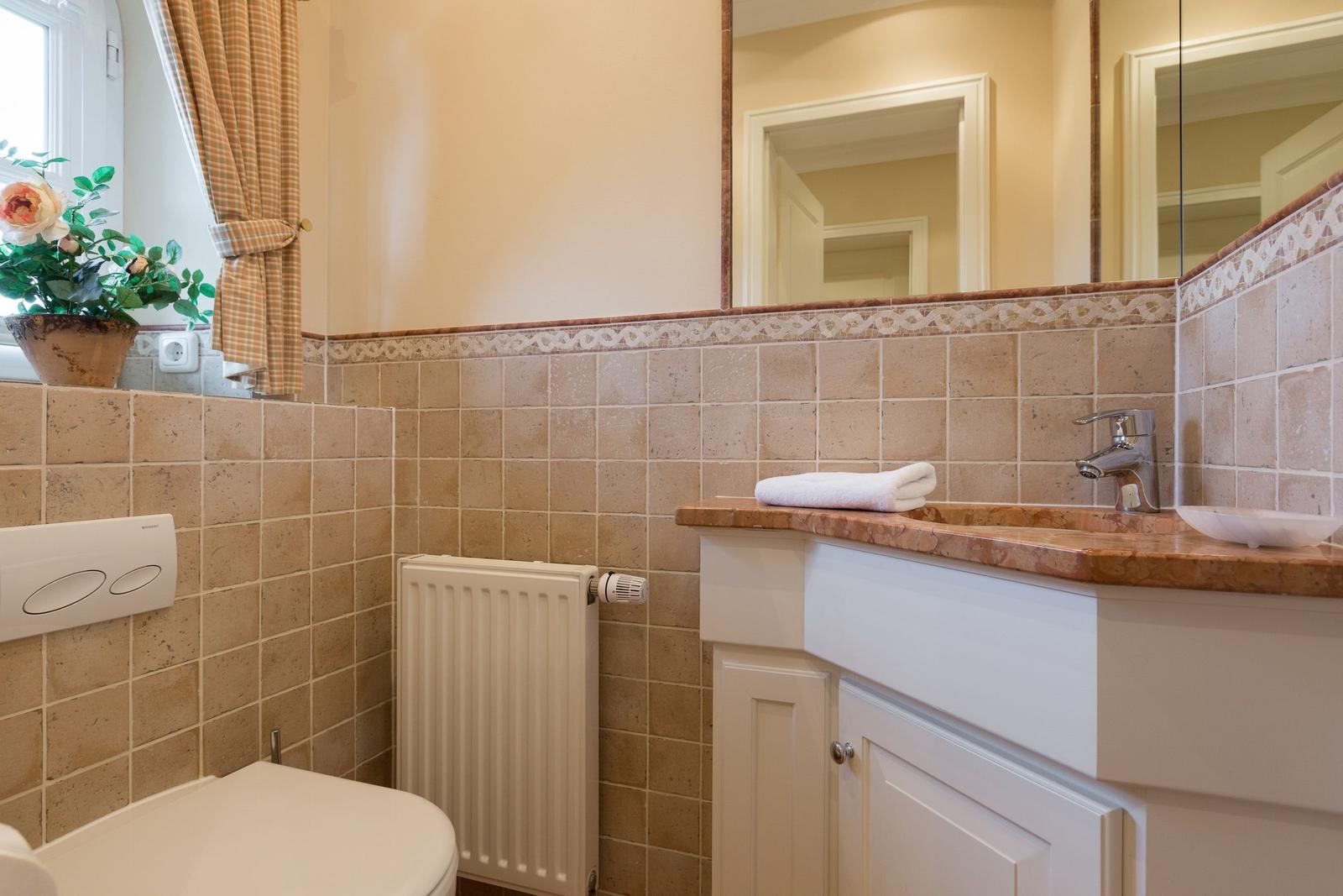 Bathroom with sink, mirror, and toilet. Walls covered with stone tiles.