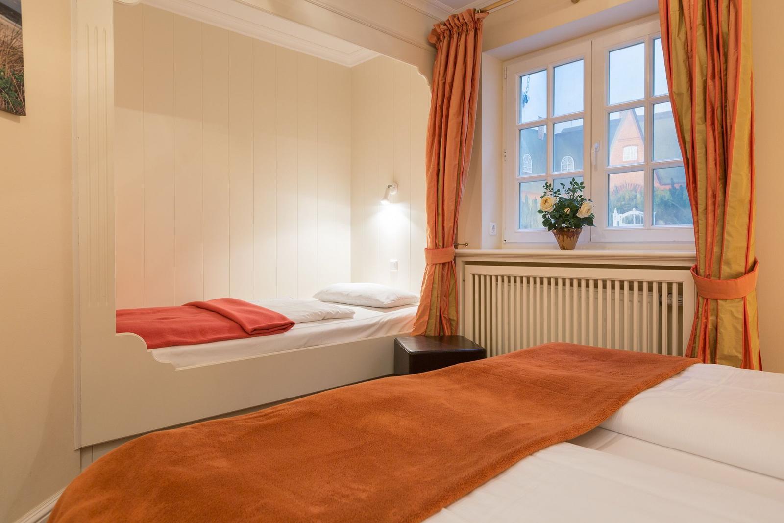 Room with two beds, window with curtains and flowers on the windowsill.