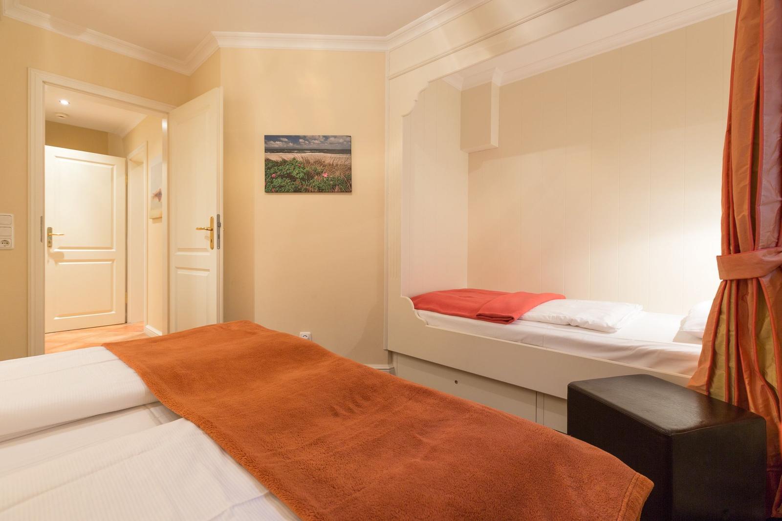 Room with two beds, wall picture, and door in background.