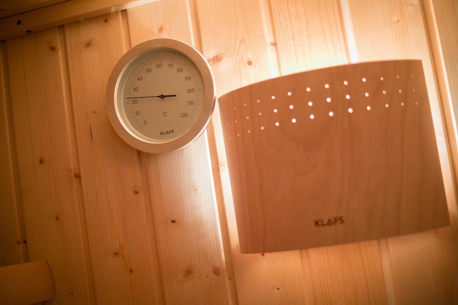Sauna with wooden wall, thermometer, and heater.