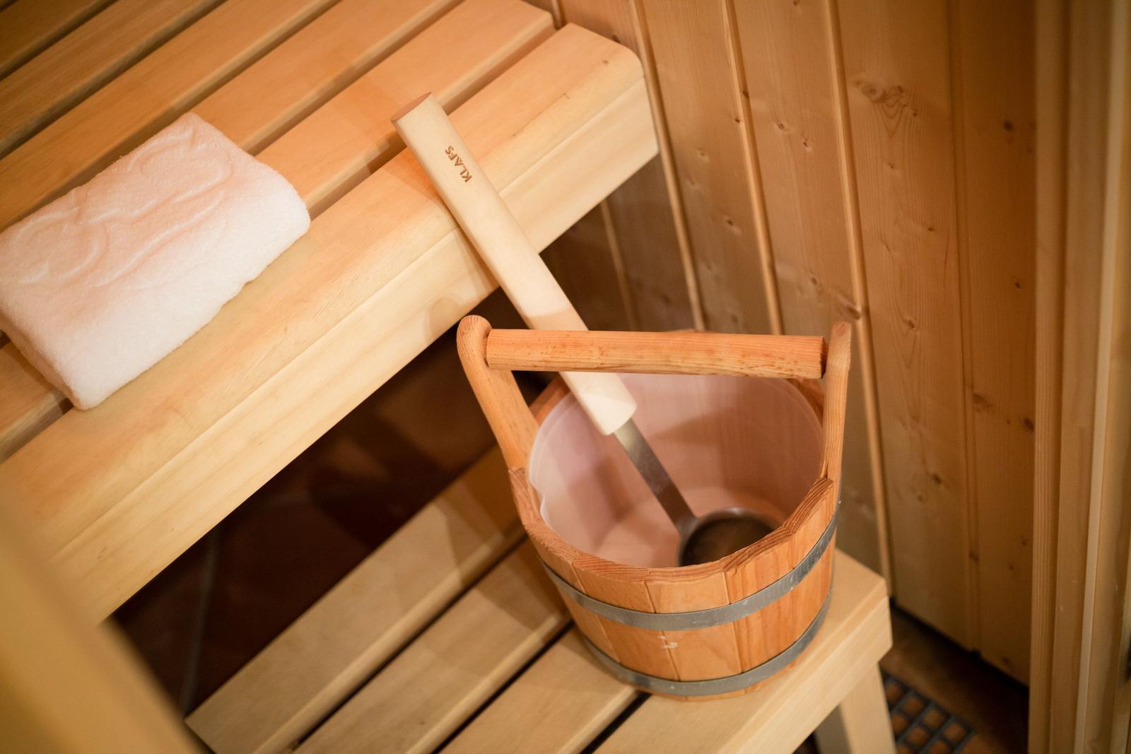Sauna with wooden bench, white towel, and bucket with ladle.