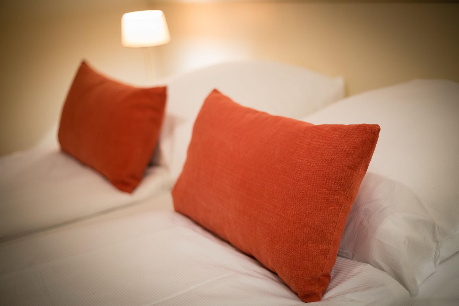 Headboard with two orange pillows and a bedside lamp.