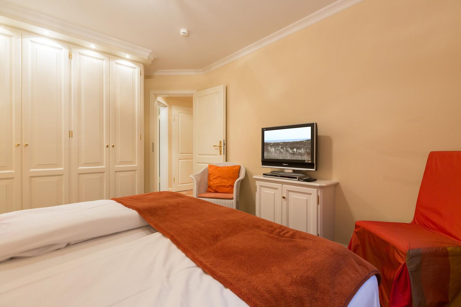 Bedroom with bed, wardrobe, TV and armchair.