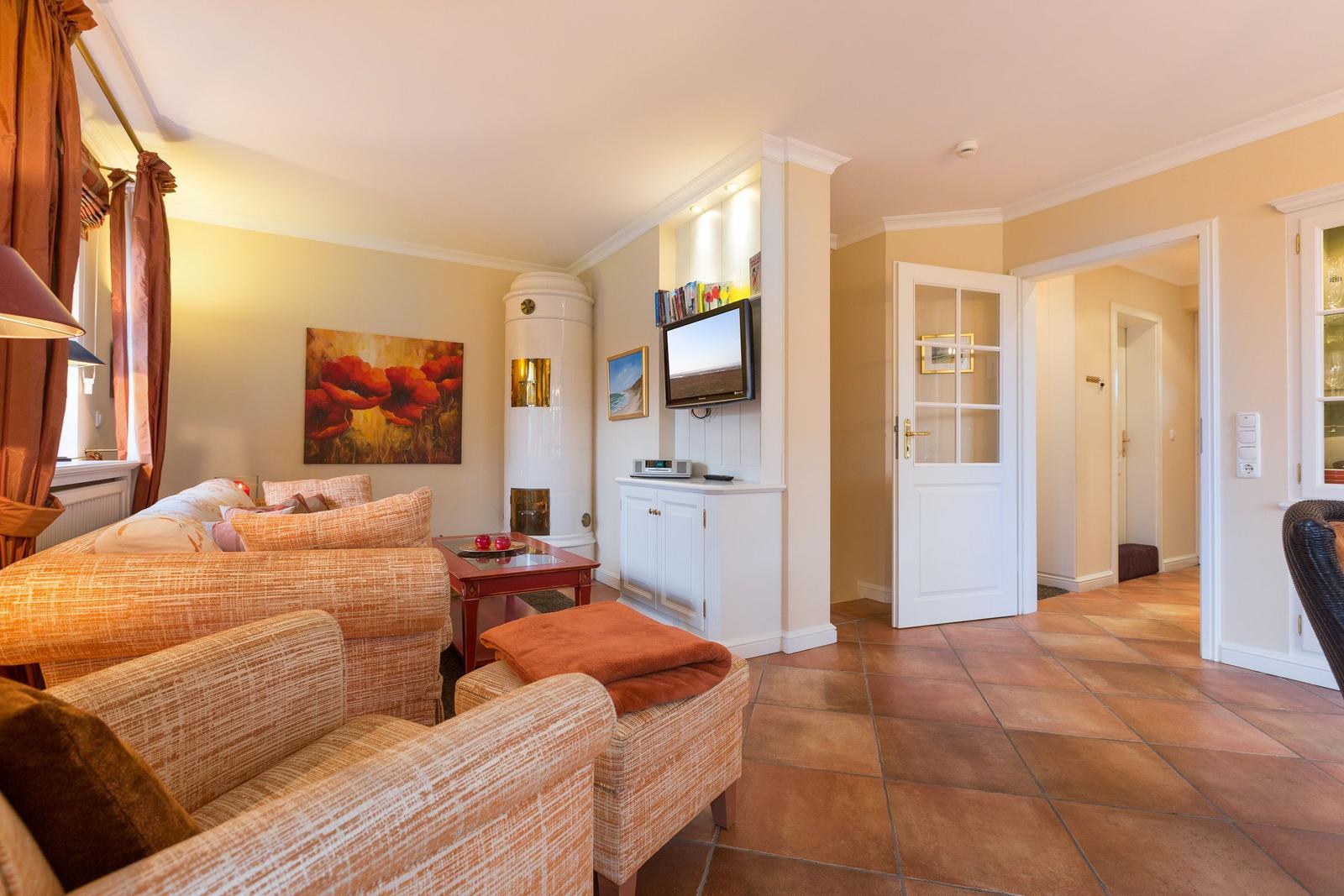 Living room with sofa, TV, and wood stove. Terracotta floor and light walls.