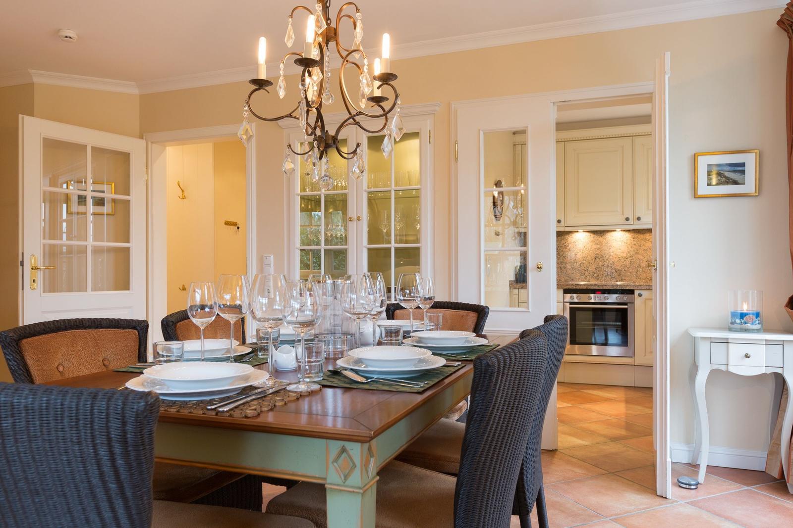 Dining room with set table and chandelier. Kitchen visible in background.