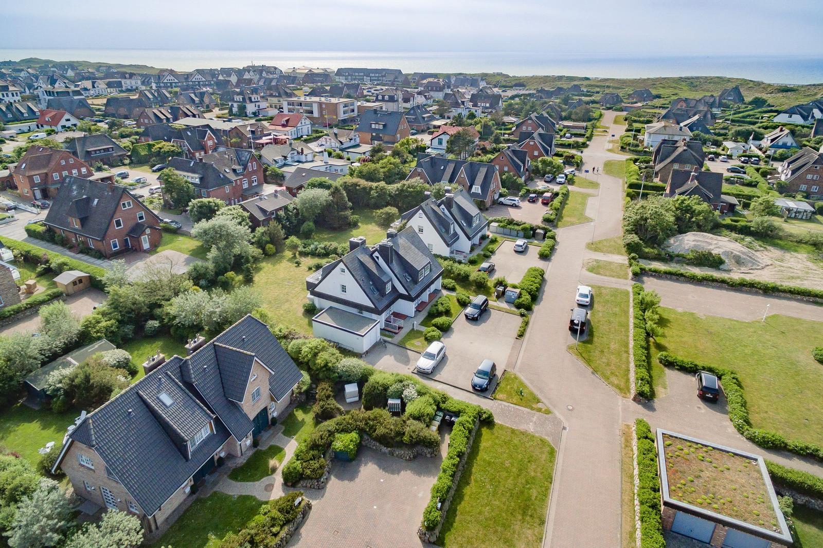 Aerial view of a coastal village with houses, gardens, and roads near the sea.