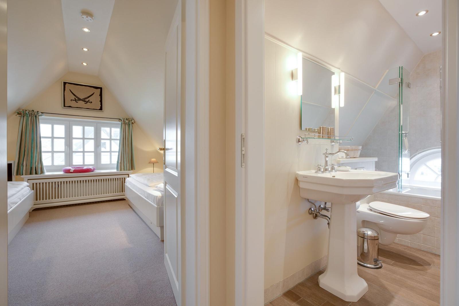 Bedroom with sloped ceiling and bathroom with pedestal sink.