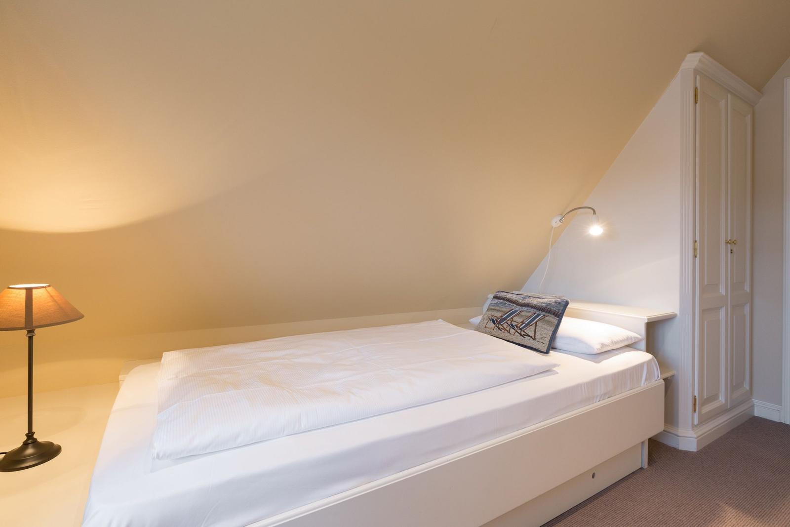 Bedroom with bed, table lamp, and wardrobe under sloped ceiling.