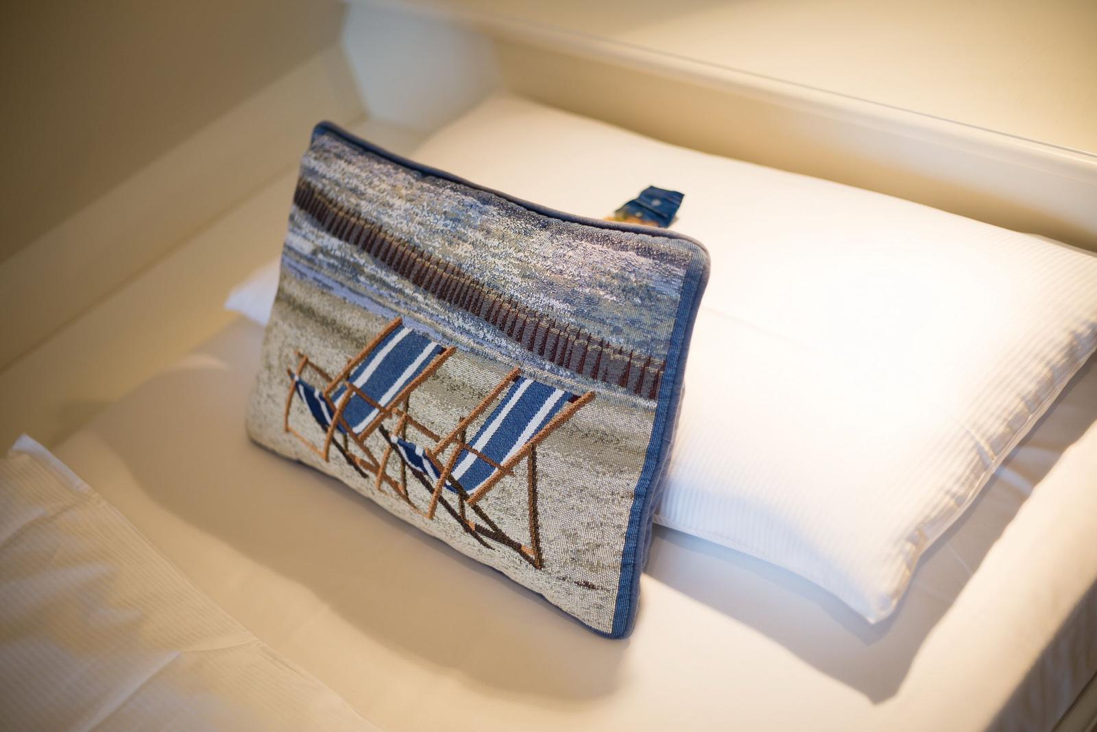 Pillow with beach motif on bed with white linens