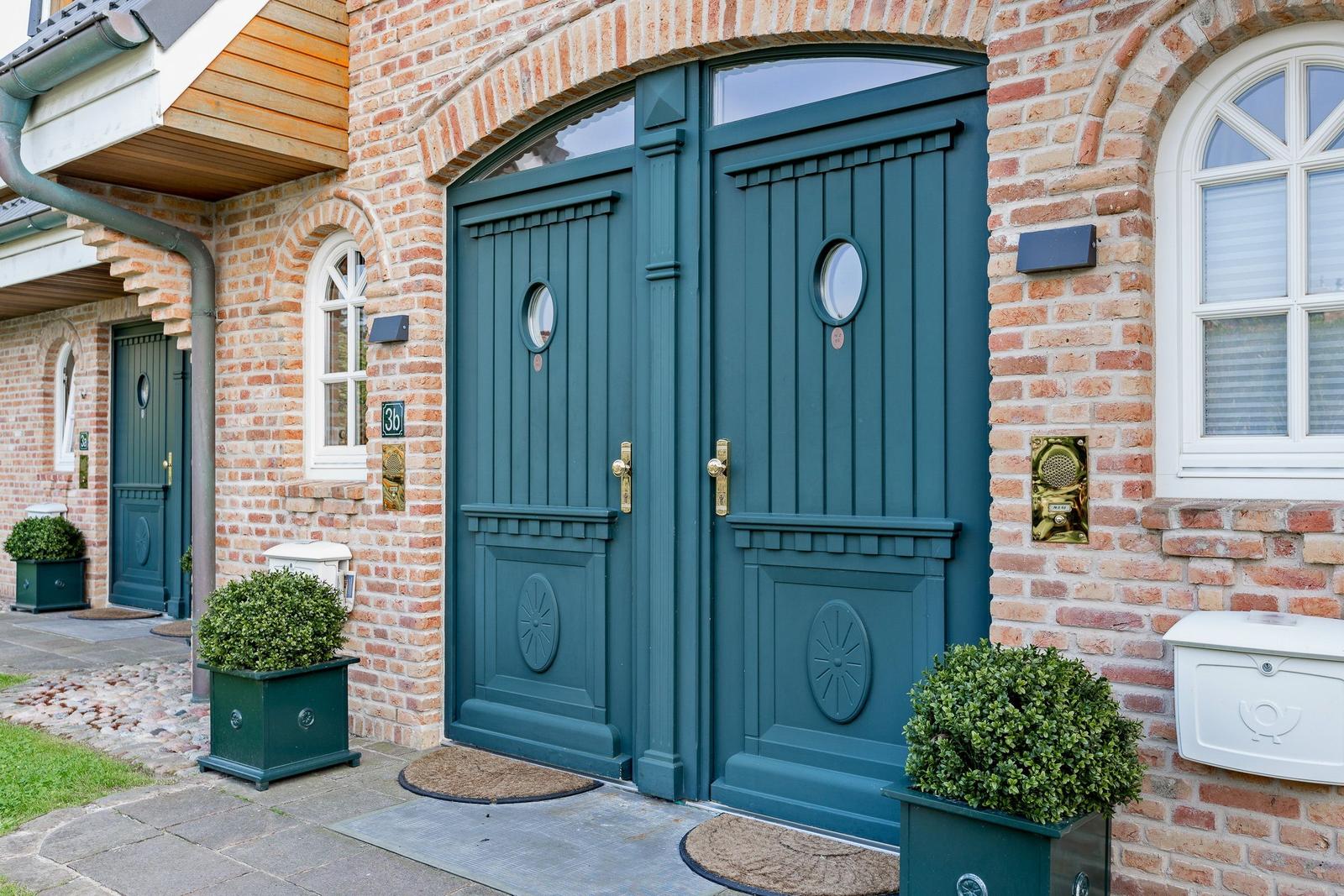 Two green front doors with round windows on a brick facade.