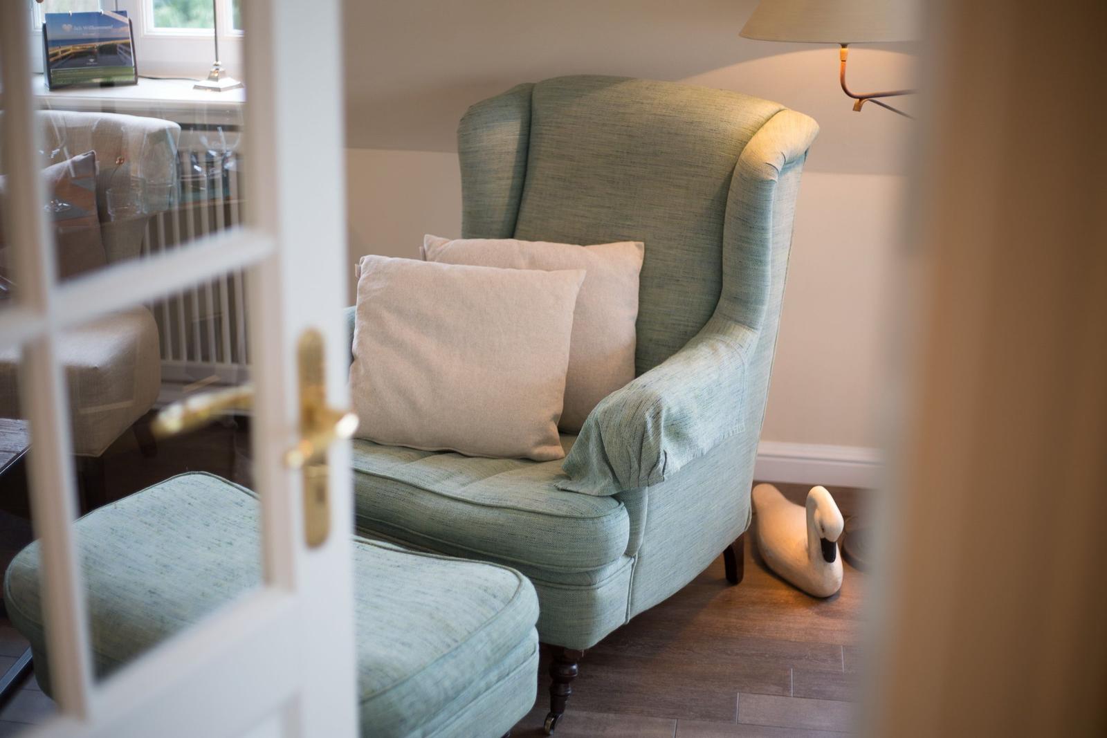 A green armchair with cushions and ottoman next to a lamp.