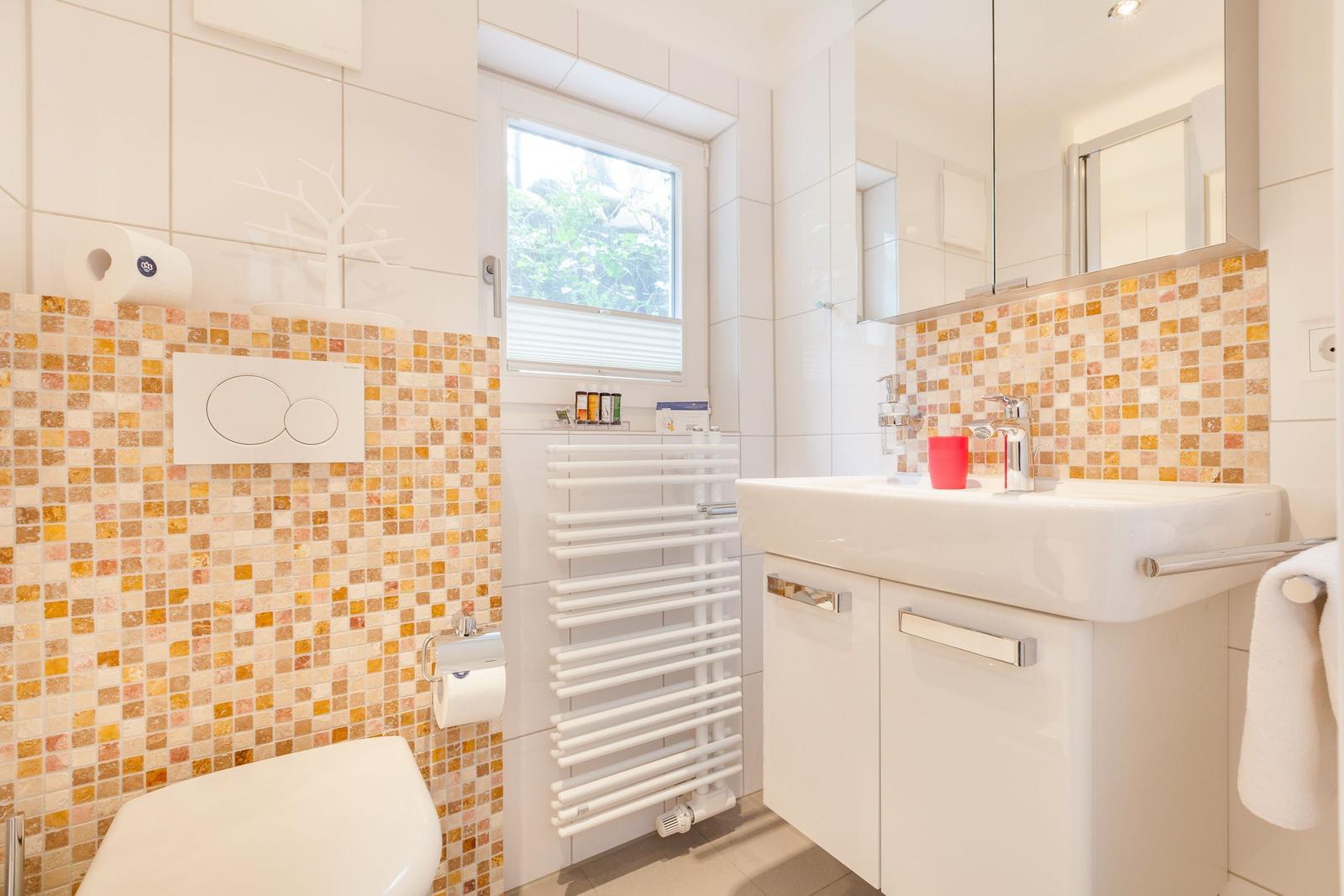 Badezimmer mit Waschbecken, Spiegel, Toilette und Fenster