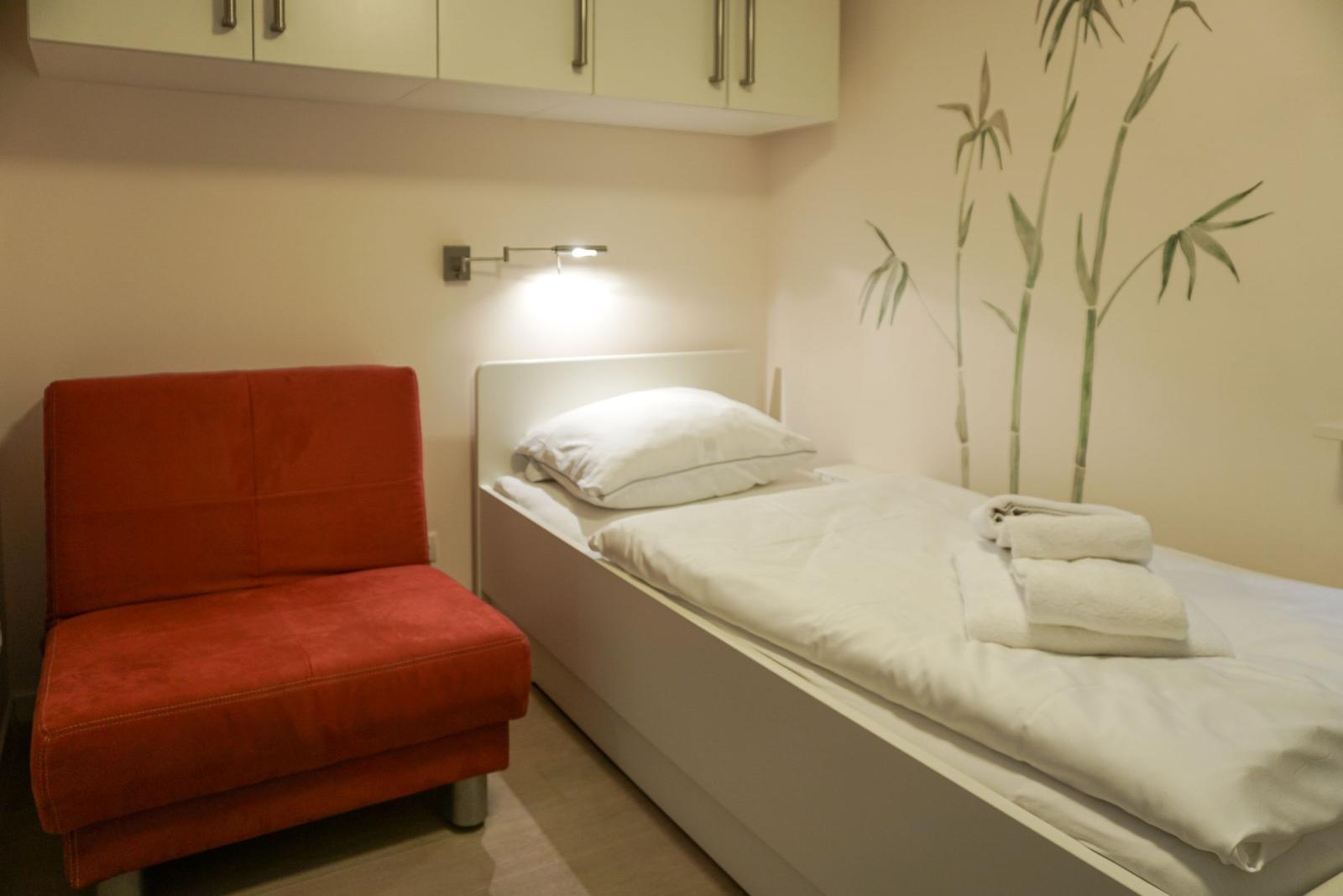 Schlafzimmer mit Bett, roter Sitzgelegenheit und Wanddekoration.