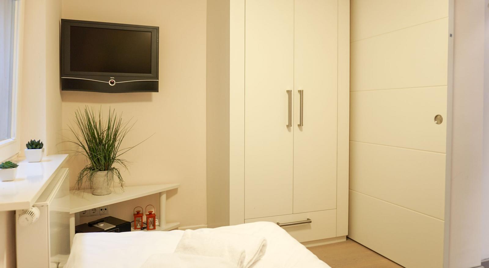 Schlafzimmer mit Bett, Kleiderschrank und Wandfernseher.