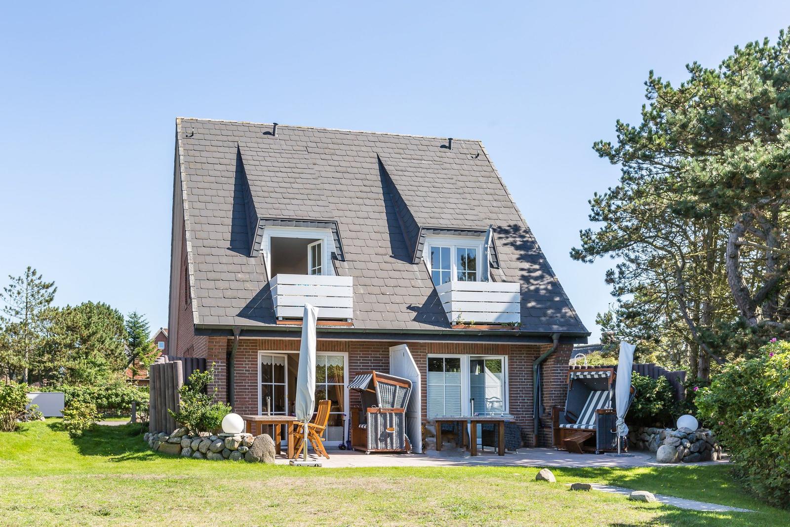 Haus mit Balkon, Terrasse und Garten. Holztische, Stühle und Sonnenschutz.