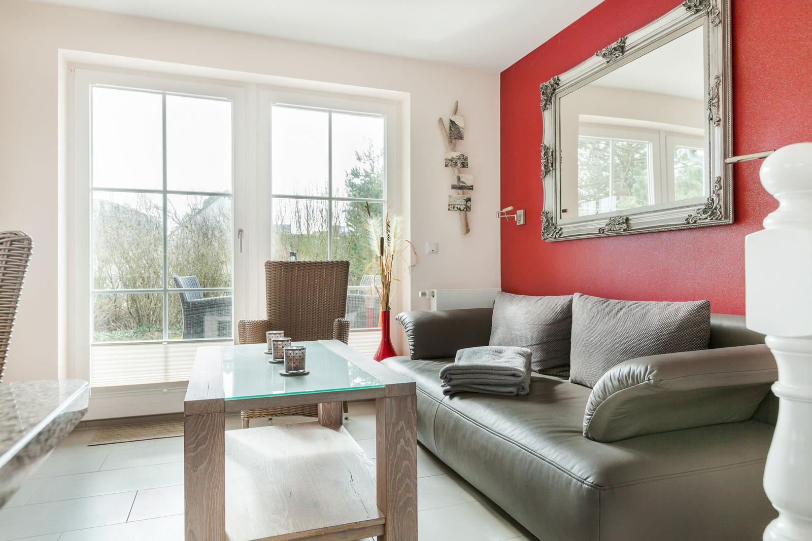 Wohnzimmer mit grauem Sofa, Glas-Tisch und roter Wand mit Spiegel.